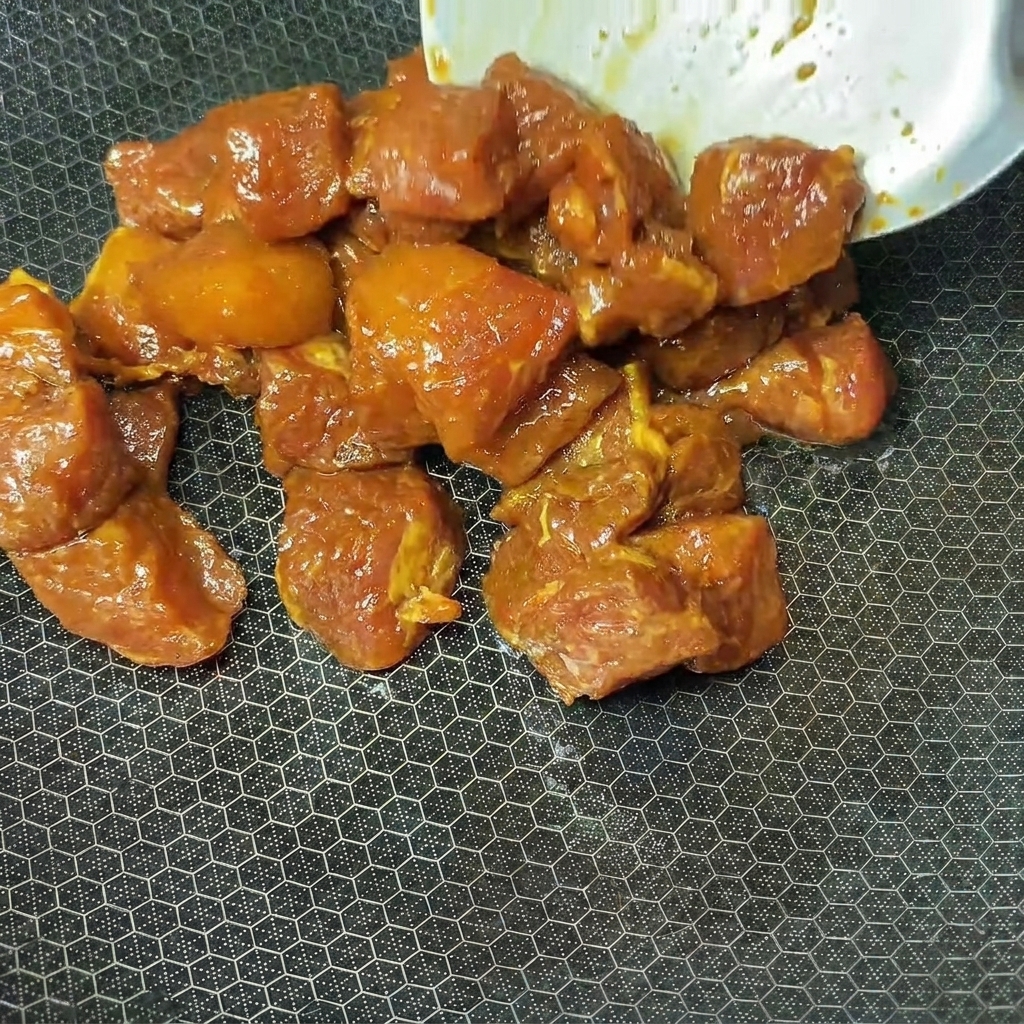 Cubos de cerdo marinados siendo colocados en un wok caliente para su cocción.