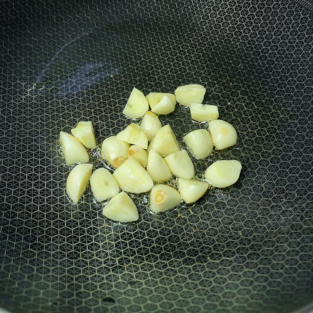 Dientes de ajo friéndose en un wok con aceite caliente.