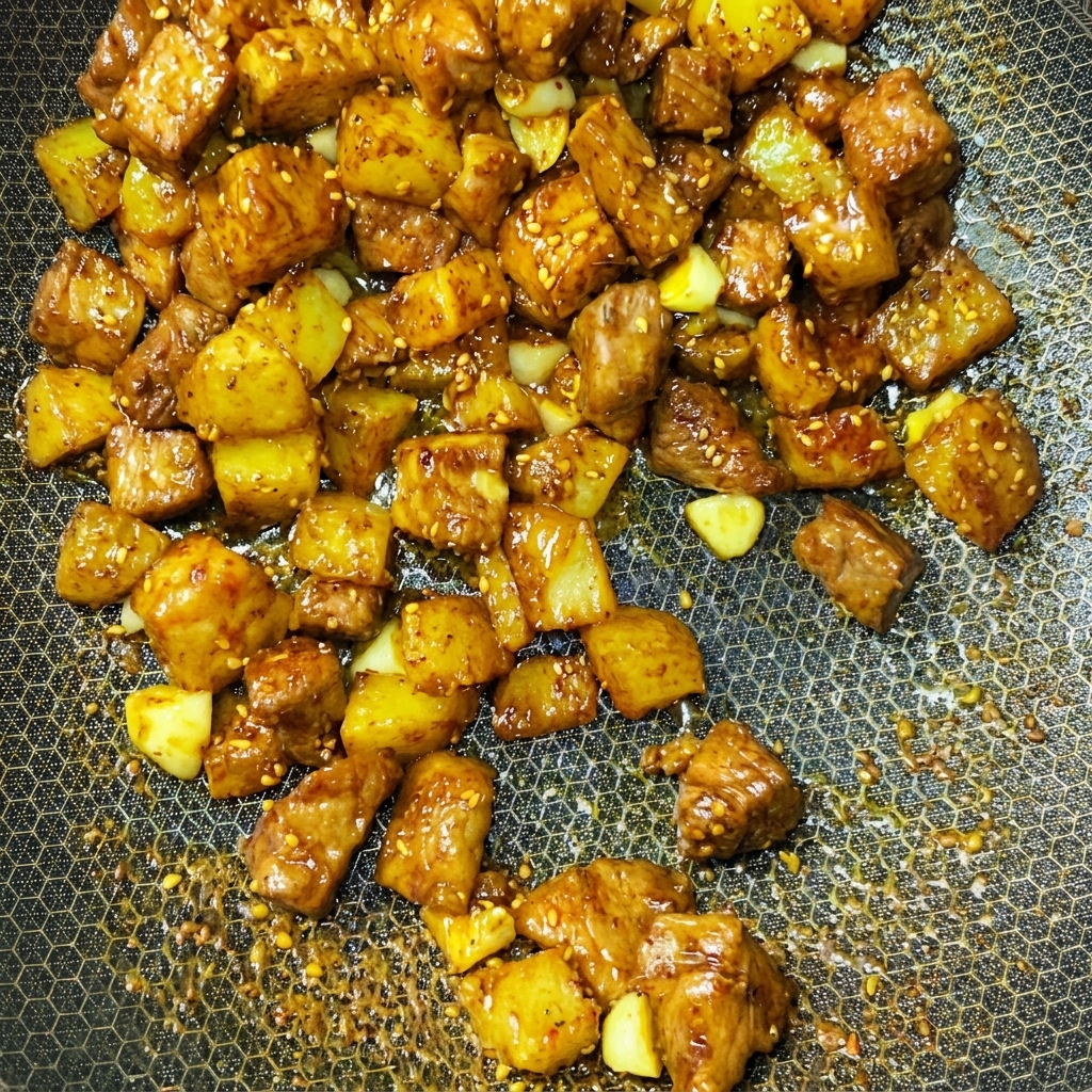 Cubos de cerdo y patata siendo salteados dinámicamente en un wok con especias.