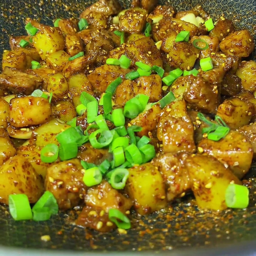 Cebollinos picados frescos espolvoreados sobre el cerdo y patatas al comino estilo barbacoa terminados en un wok.