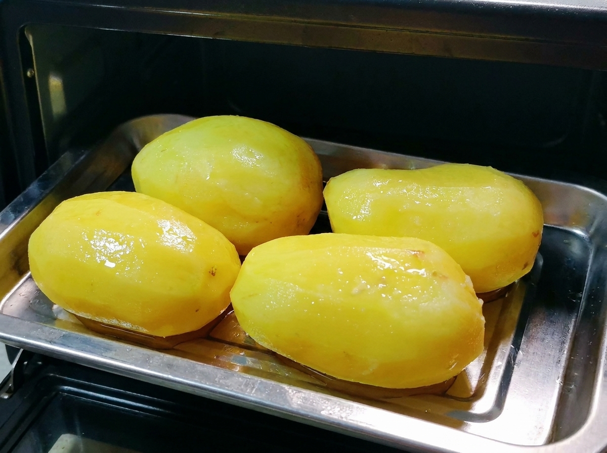 Una bandeja de metal con papas enteras aceitadas siendo colocada dentro de un pequeño horno negro.
