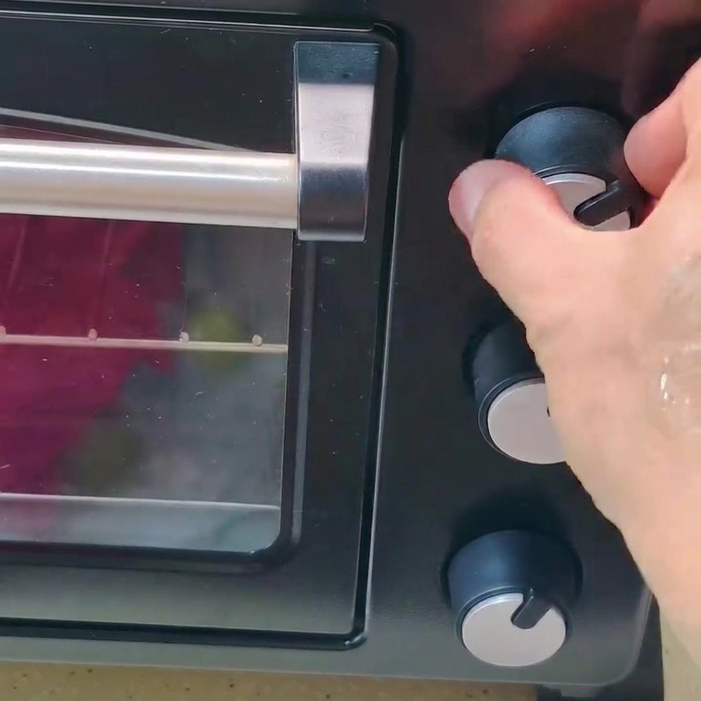 Una mano girando la perilla de control de temperatura en un horno negro.