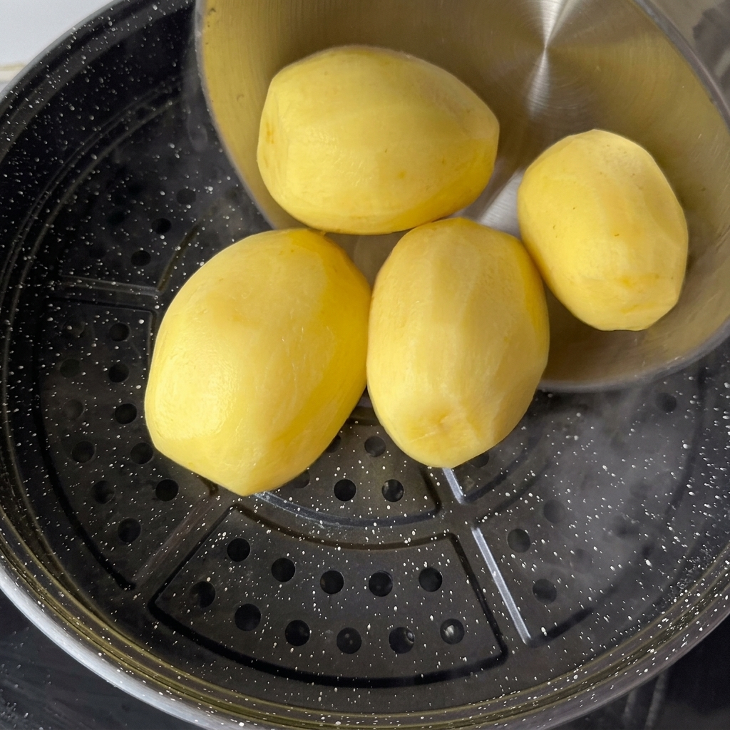 Patatas amarillas peladas colocadas en una bandeja de vapor sobre agua hirviendo.