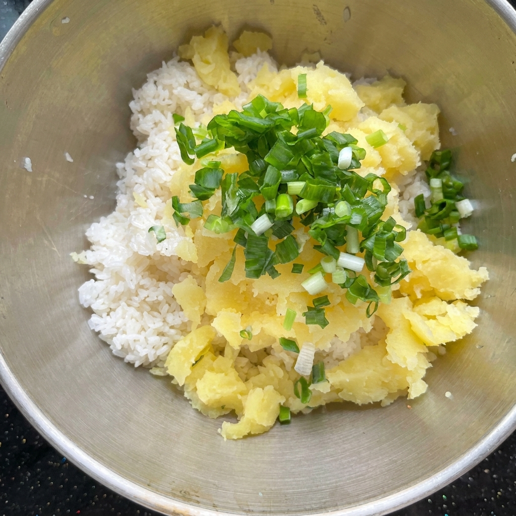 Trozos de patata horneada y condimentos combinados con arroz cocido en un bol de metal.