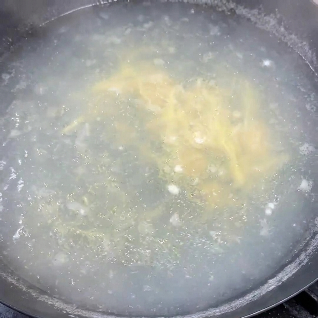 Cebollinos picados siendo revueltos uniformemente en una olla de sopa caliente a fuego lento.