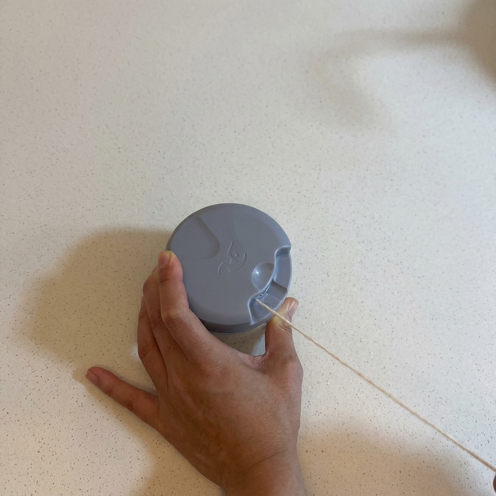 Manos operando una picadora manual de cuerda en una encimera blanca para picar ajo.