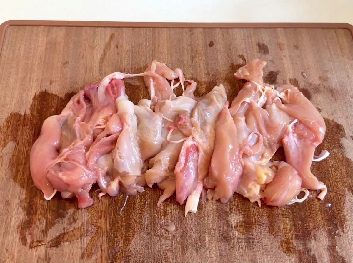 Trozo de carne de pollo cruda y deshuesada reunidos en una tabla de cortar de madera.