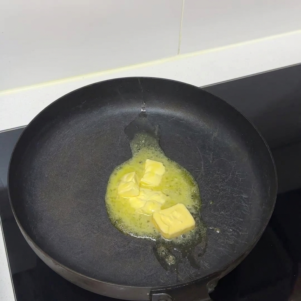 Trozos de mantequilla derritiéndose hasta convertirse en líquido en una sartén oscura sobre una estufa.