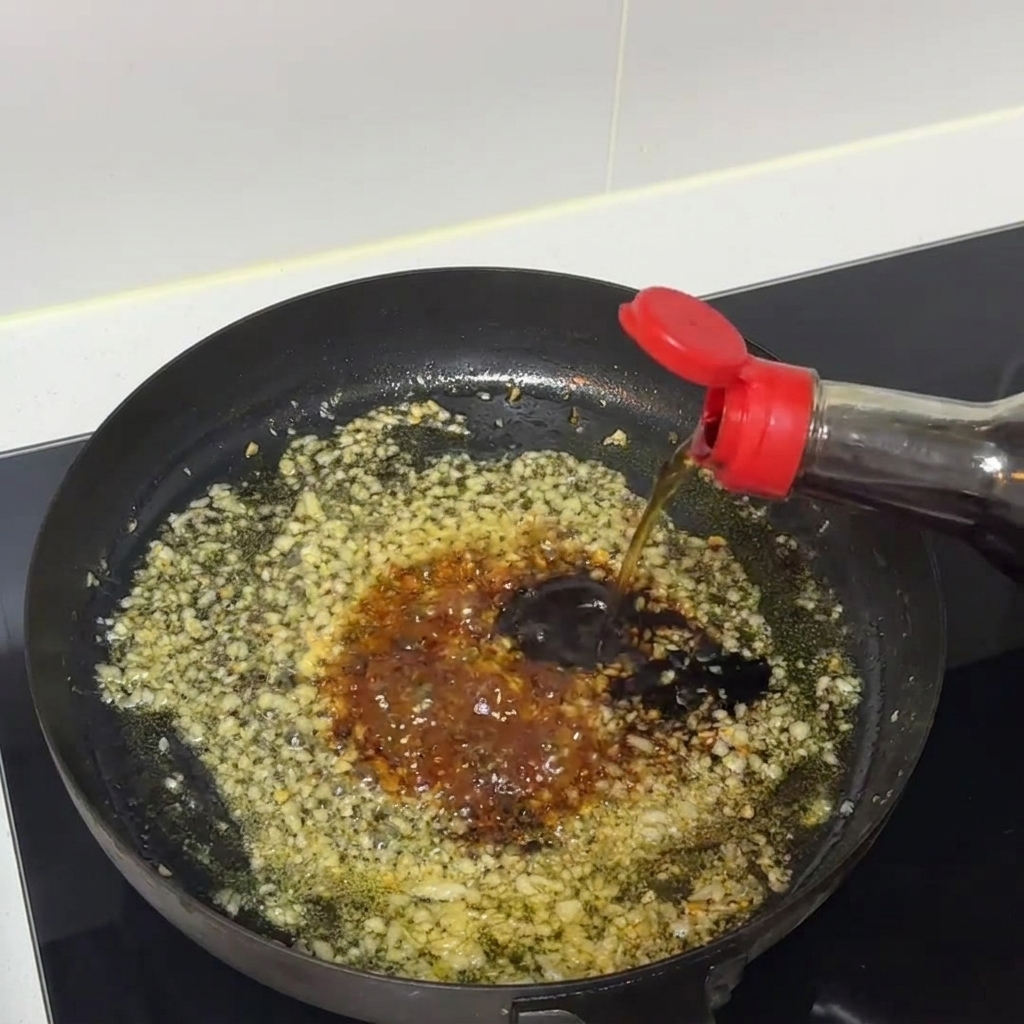 Mezcla de salsa oscura hirviendo a fuego lento y siendo revuelta dentro de una sartén con ajo picado.