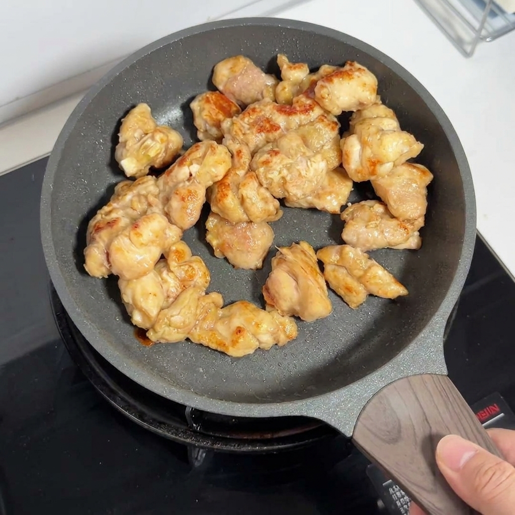 Trozos de muslo de pollo dorados friéndose dentro de una sartén antiadherente.