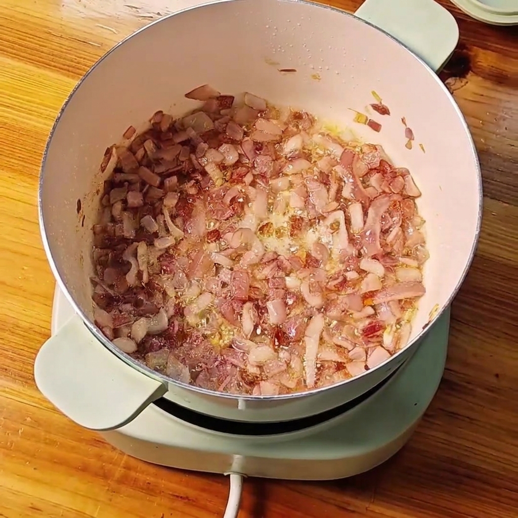 Cebollas rojas en dados sofritas en una olla con ajo picado y jengibre mezclándose juntos.