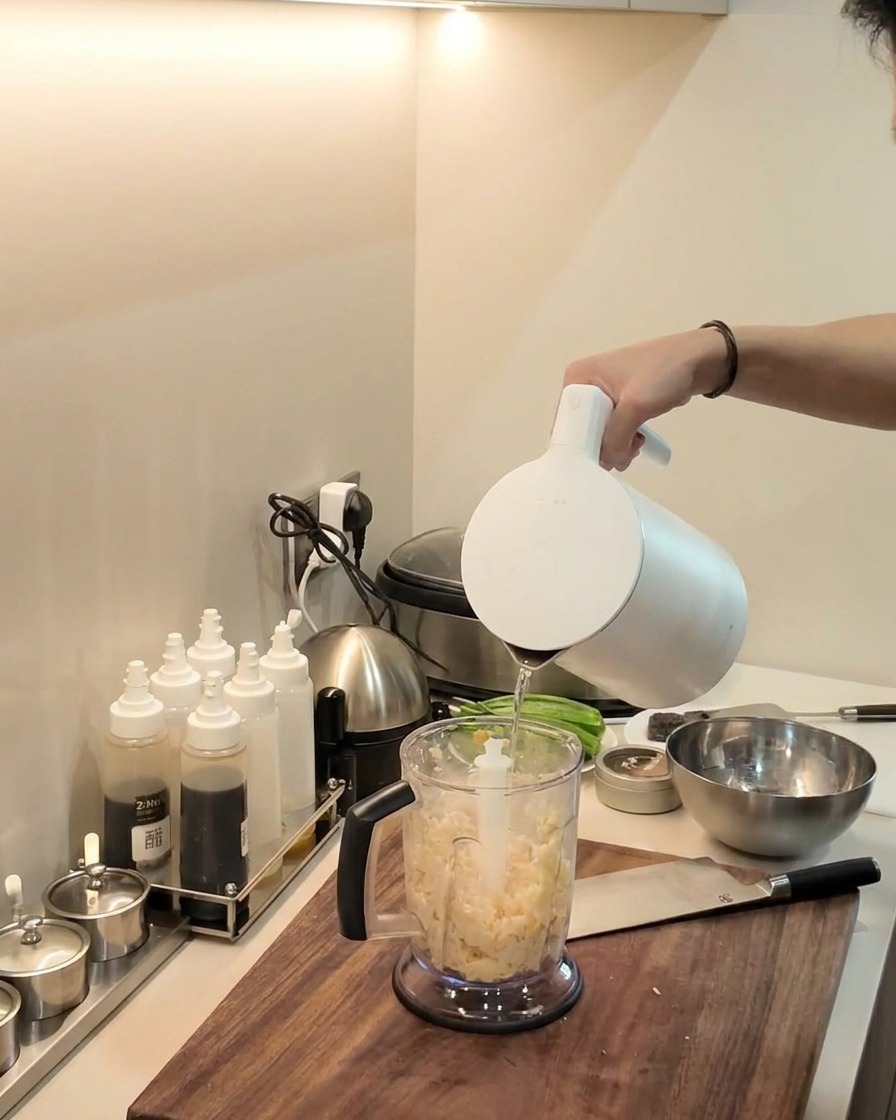 Una batidora de inmersión haciendo puré la mezcla de yuca y plátano dentro del vaso de la licuadora.