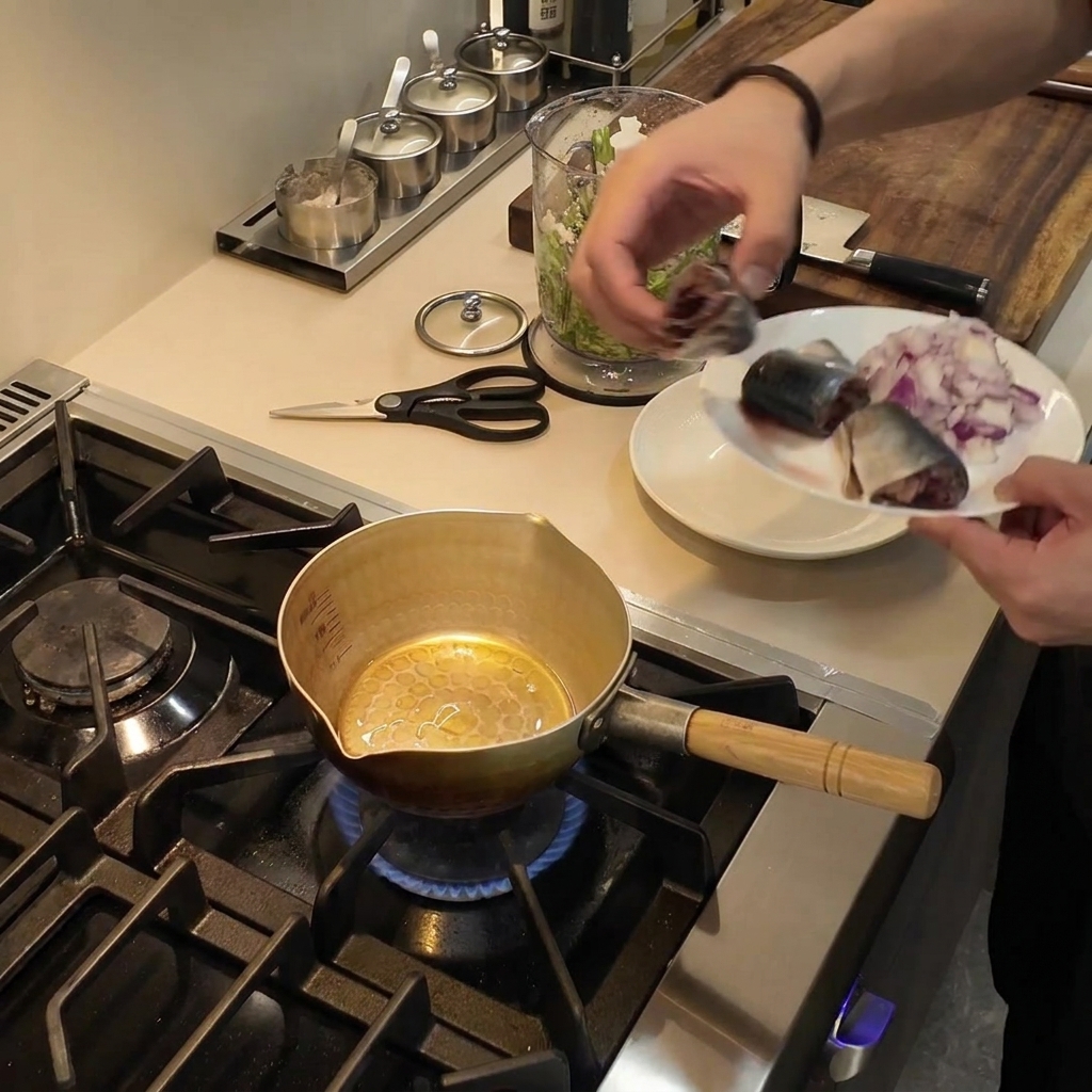 Una pequeña olla dorada sobre un quemador de gas con aceite de cocina brillando en su interior.