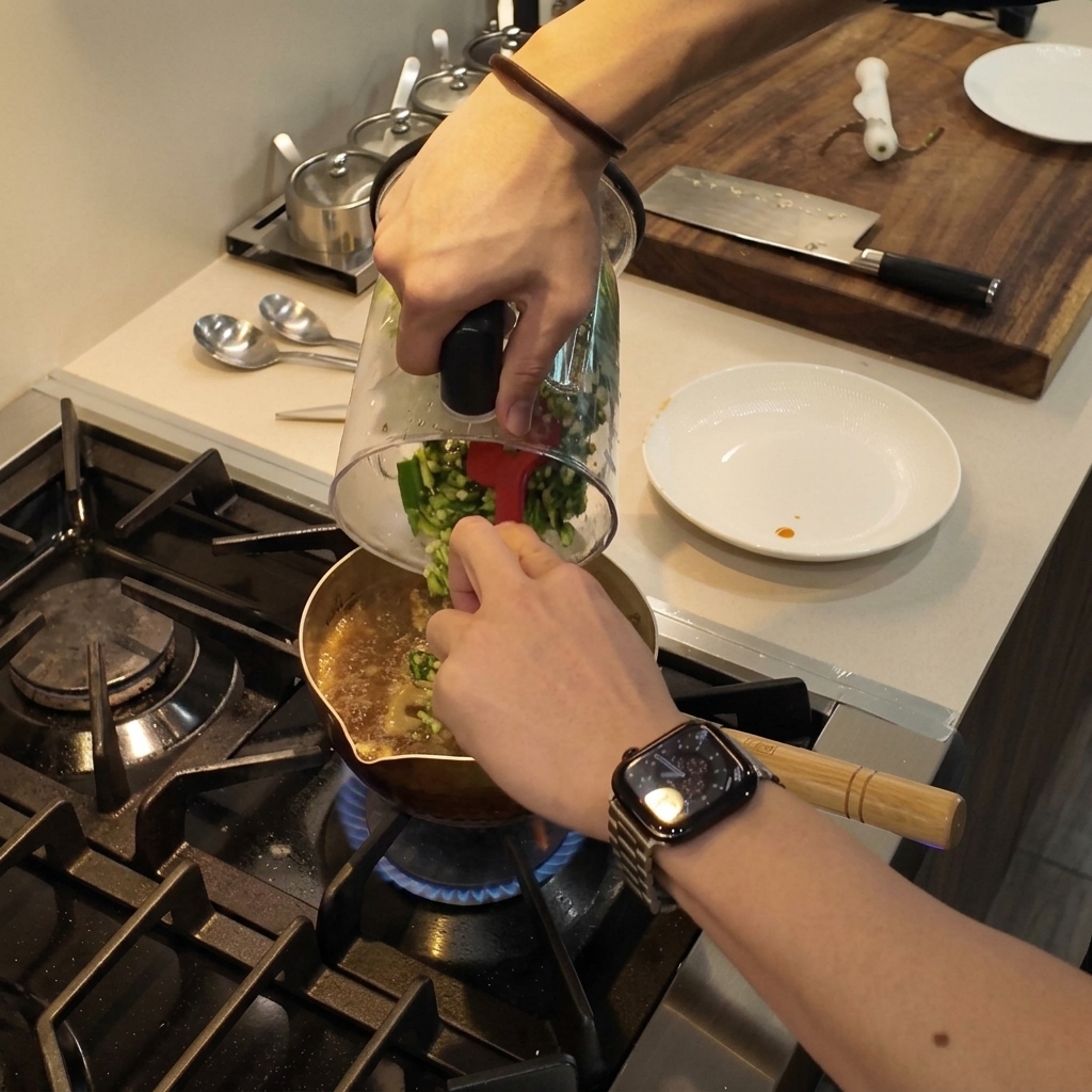 Okra verde picada siendo retirada de un vaso de licuadora hacia una olla de estofado a fuego lento utilizando una espátula roja.