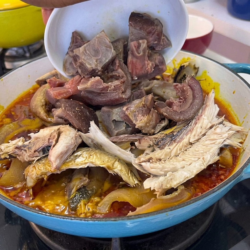 Trozos de carne de cerdo cocida siendo vertidos desde un tazón hacia la olla que contiene el pescado y la salsa.