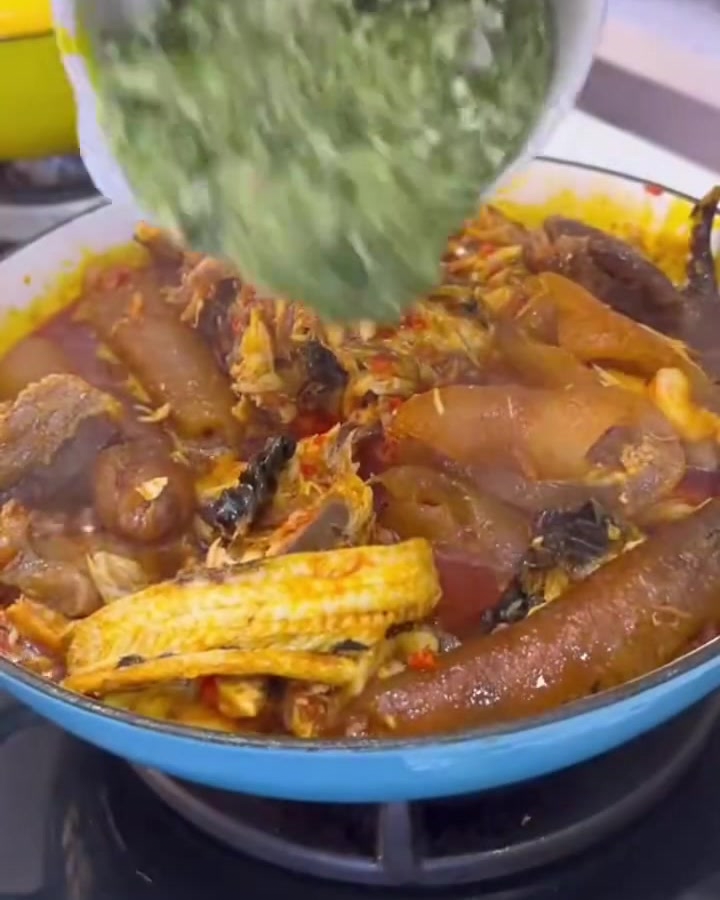 Okra verde finamente picada siendo vertida desde un tazón blanco en una rica olla burbujeante de carnes y salsa.