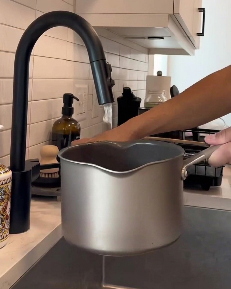 Manos revolviendo arroz blanco en una olla de metal bajo un grifo de cocina con agua corriente.