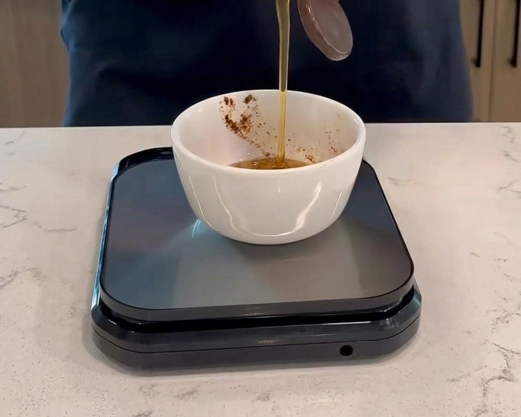Vertiendo miel de una botella de plástico en un pequeño tazón blanco con salsa roja oscura, colocado sobre una báscula de cocina digital.