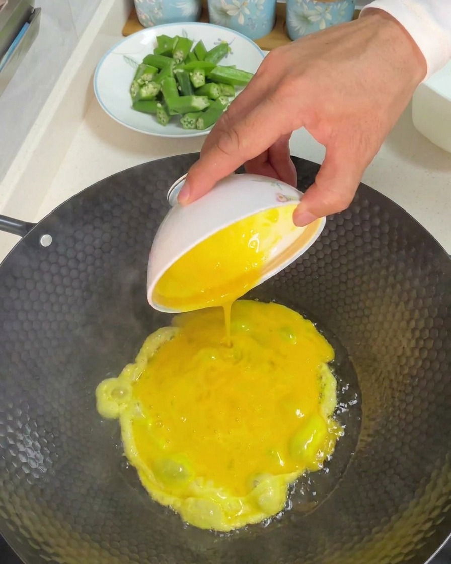 Vertiendo un bol de huevos batidos amarillos en un wok caliente con aceite.