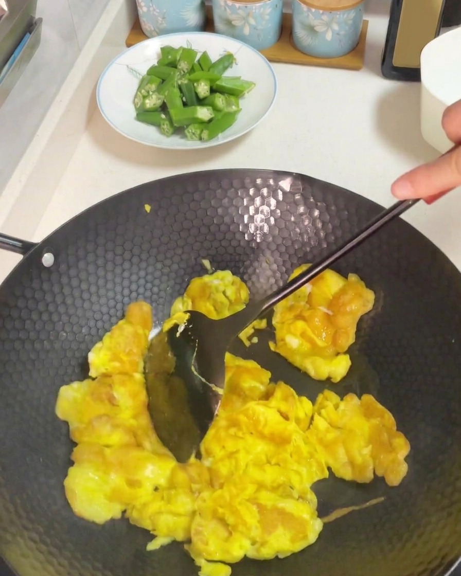 Usando una espátula oscura para remover y revolver los huevos cocinados en un wok caliente.