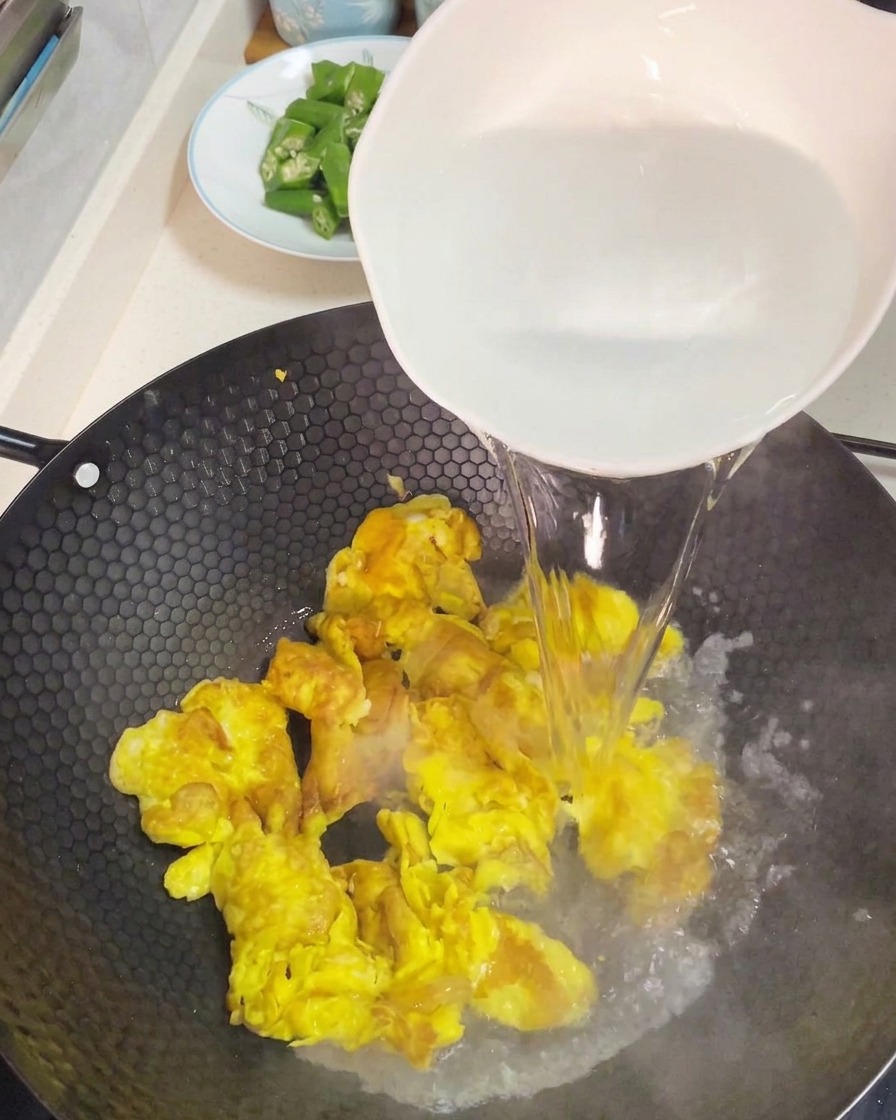 Vertiendo agua muy caliente de un cuenco blanco grande sobre los huevos revueltos para crear una base de sopa.