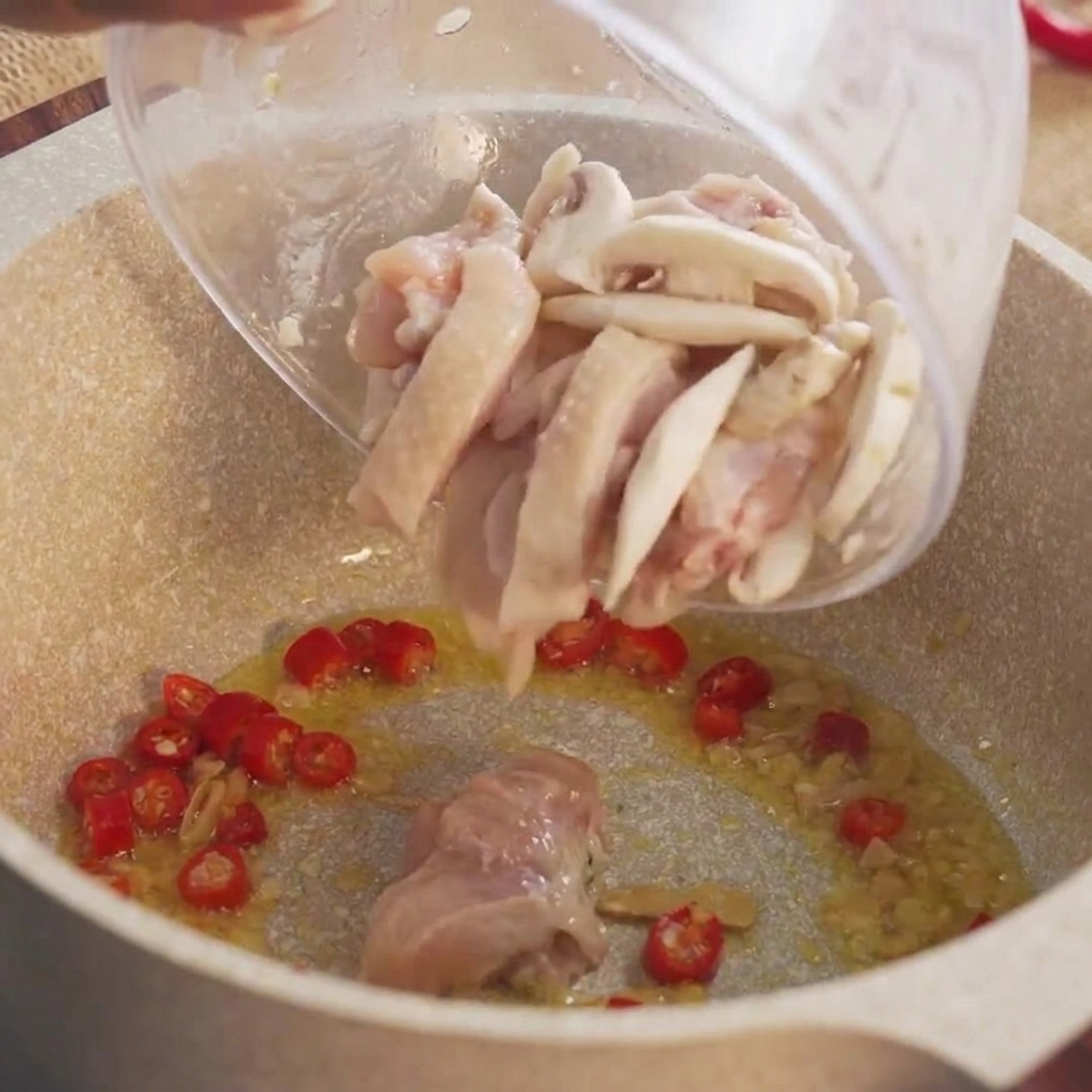 Trozos marinados de pollo crudo siendo vertidos desde un bol hacia la olla caliente.