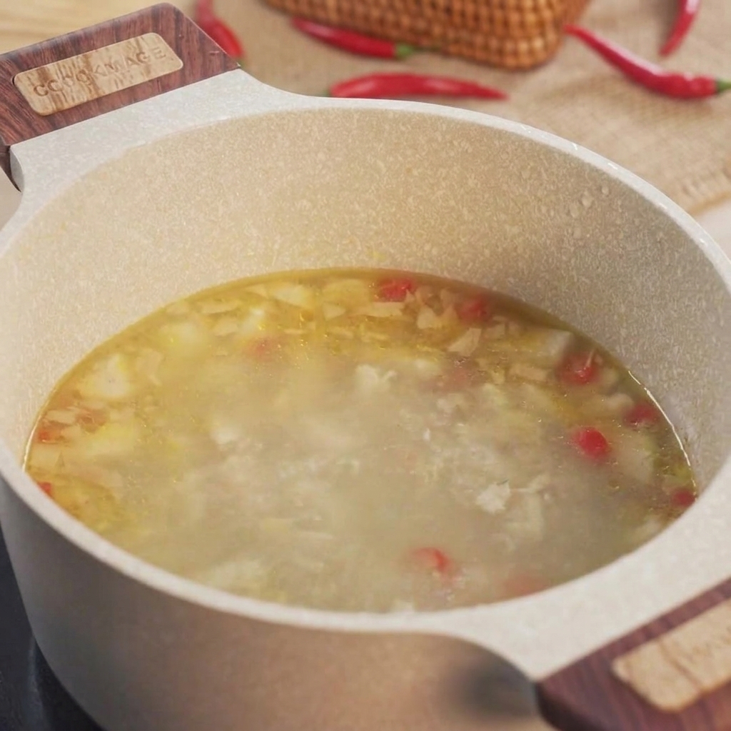 Rodajas de okra verde siendo añadidas a una olla llena de caldo de pollo hirviendo a fuego lento.