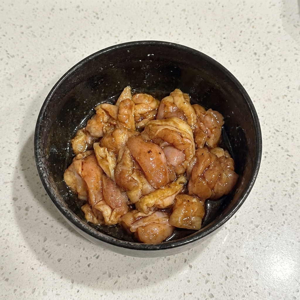 Trozos de pollo crudo marinado mezclados en un bol negro.