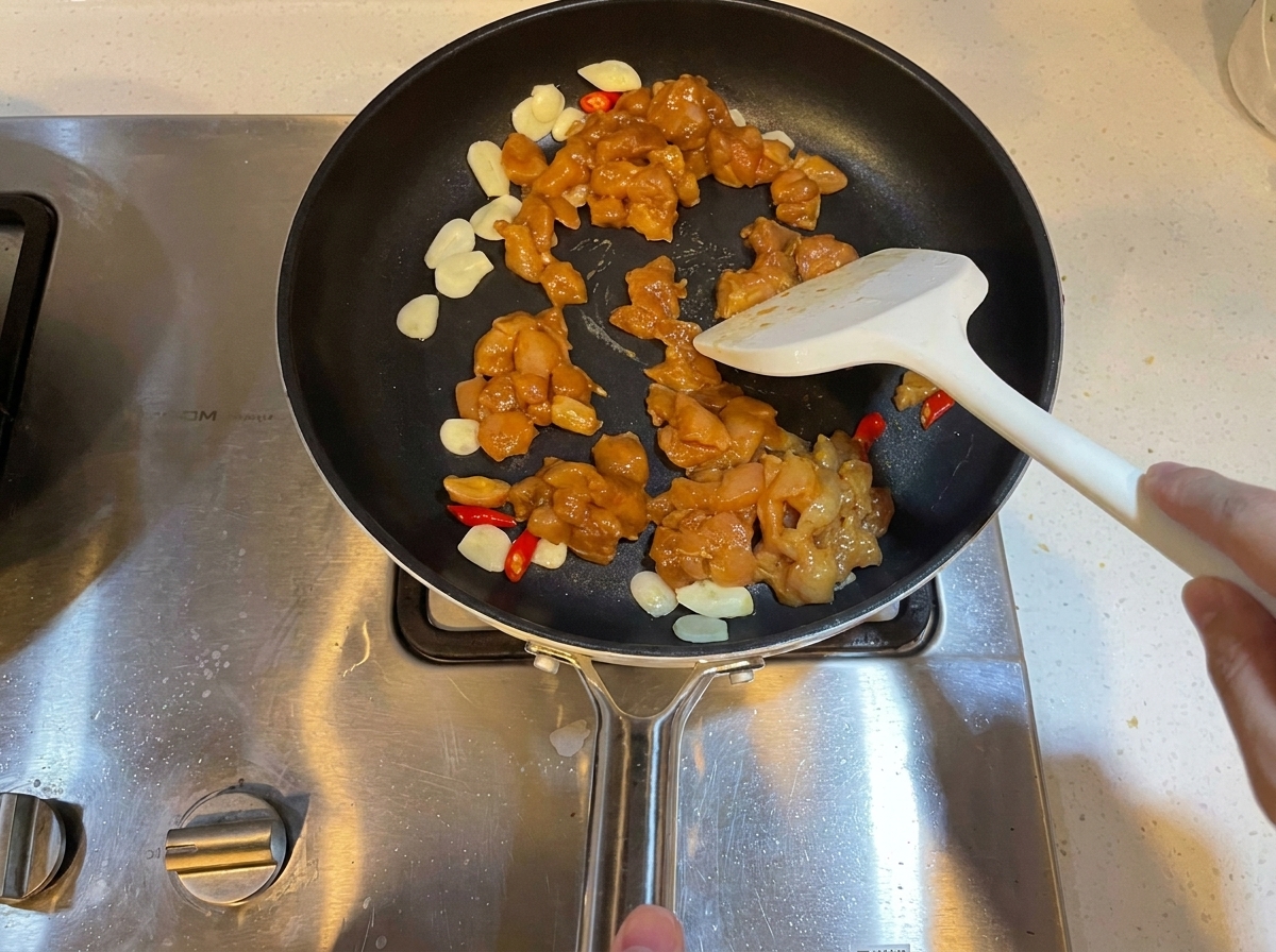 Dados de pollo marinado salteándose en una sartén con ajo y chiles.