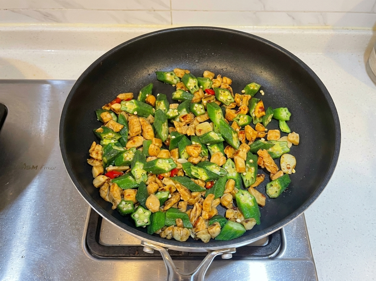 Añadiendo salsa de ostras al salteado de pollo y okra en la sartén.