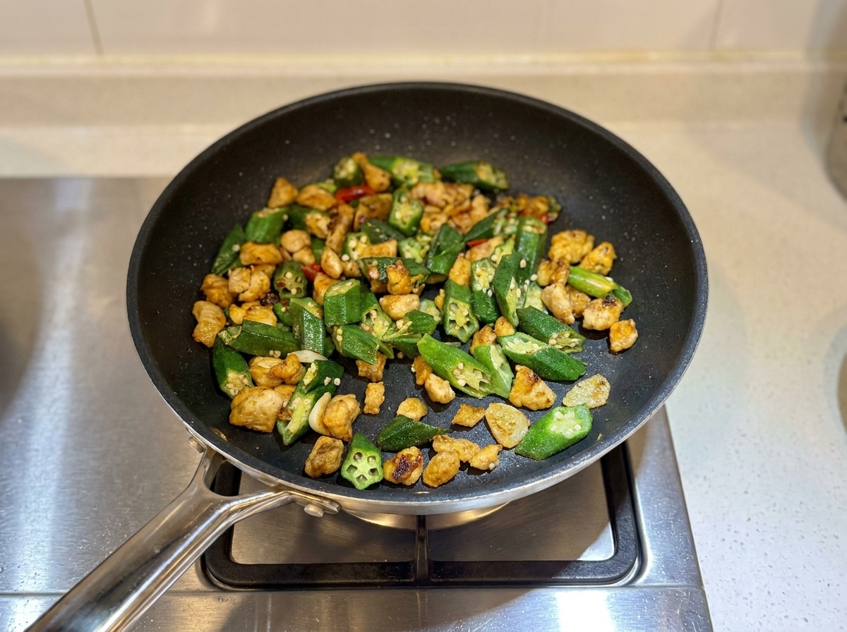 Salteado de pollo y okra terminado en la sartén, con un aspecto ligeramente seco y listo para servir.