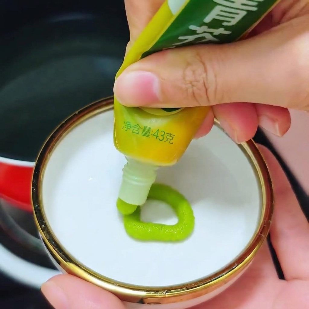 Una persona exprimiendo un anillo de pasta de wasabi verde brillante de un tubo en un pequeño plato blanco.