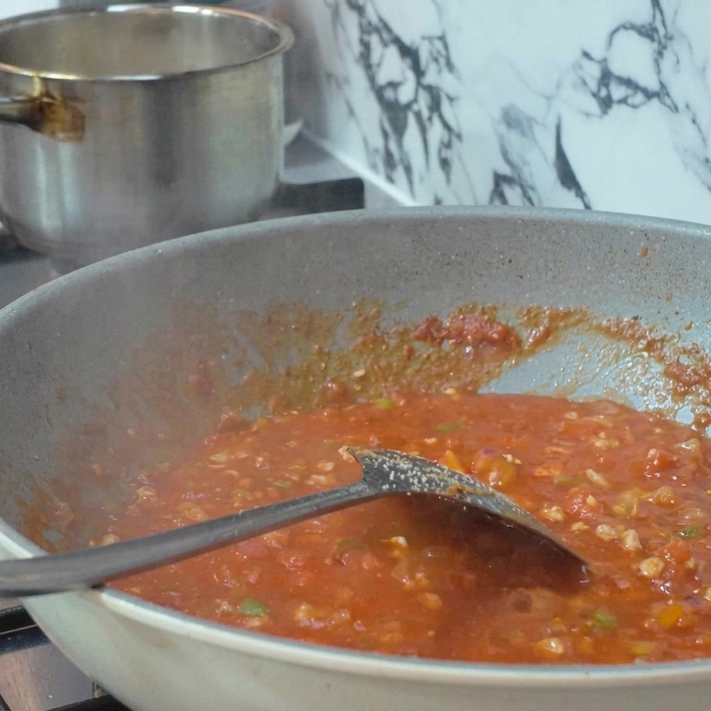 Tomates frescos sujetos en brochetas metálicas y asados directamente sobre la llama azul de un quemador de gas.