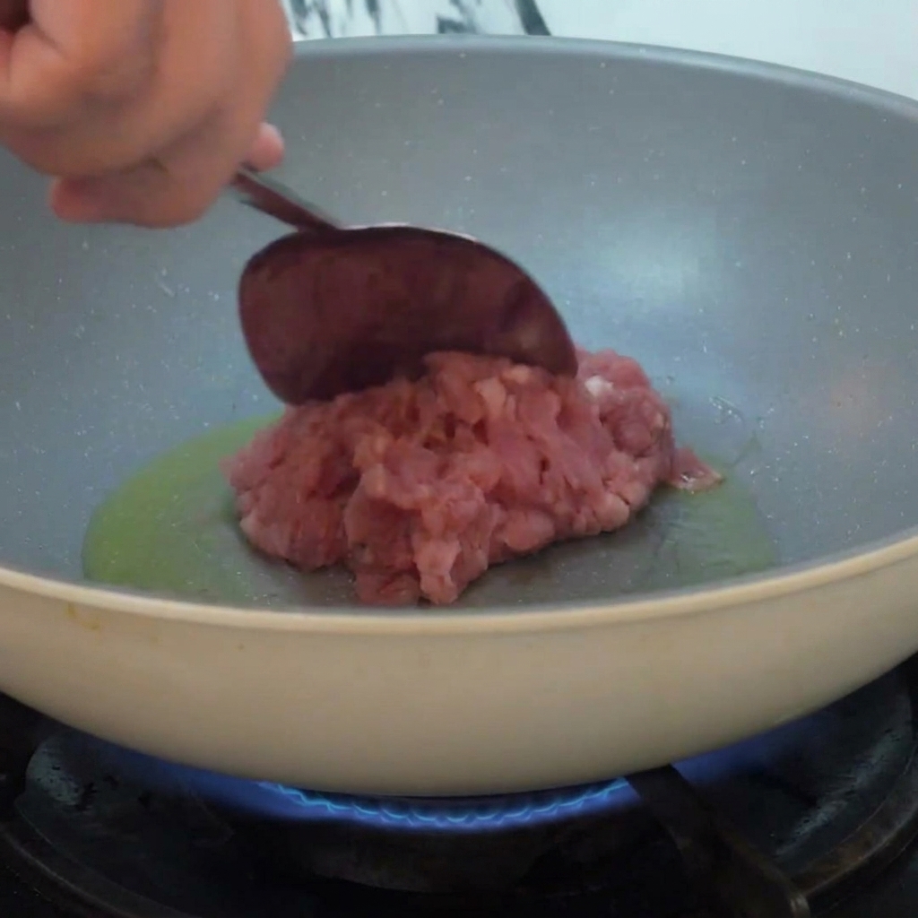Carne picada siendo añadida a una sartén con aceite caliente y salteada sobre la llama.