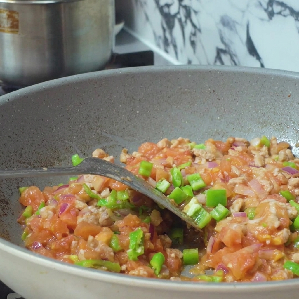 Agua siendo vertida desde un recipiente en una sartén llena de una mezcla de carne picada y verduras en dados.