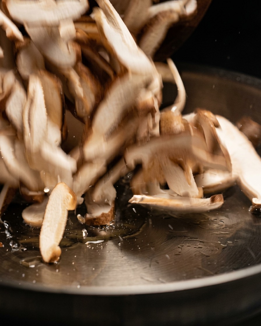 Rodajas de champiñón crudo siendo salteadas y agregadas a una sartén caliente.