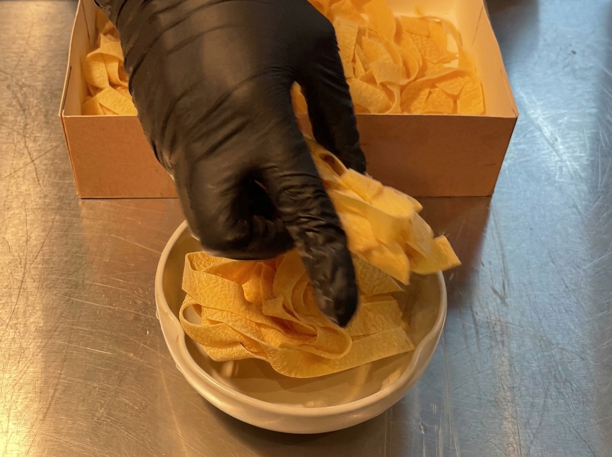 Fideos de pasta anchos porcionados desde una caja de cartón hacia un bol de cocina.