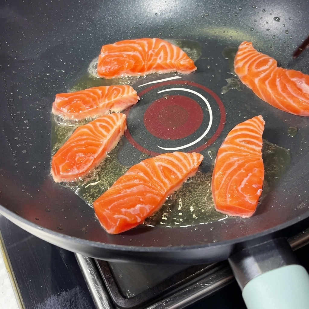 Varios trozos de salmón chisporroteando en una sartén caliente dispuestos en un patrón circular, siendo colocados con palillos.