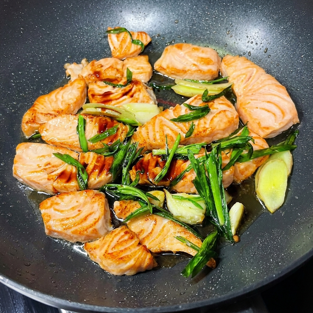 Trozos de salmón en una sartén cubiertos con salsa de soja y decorados con cebollines verdes frescos y semillas de sésamo.
