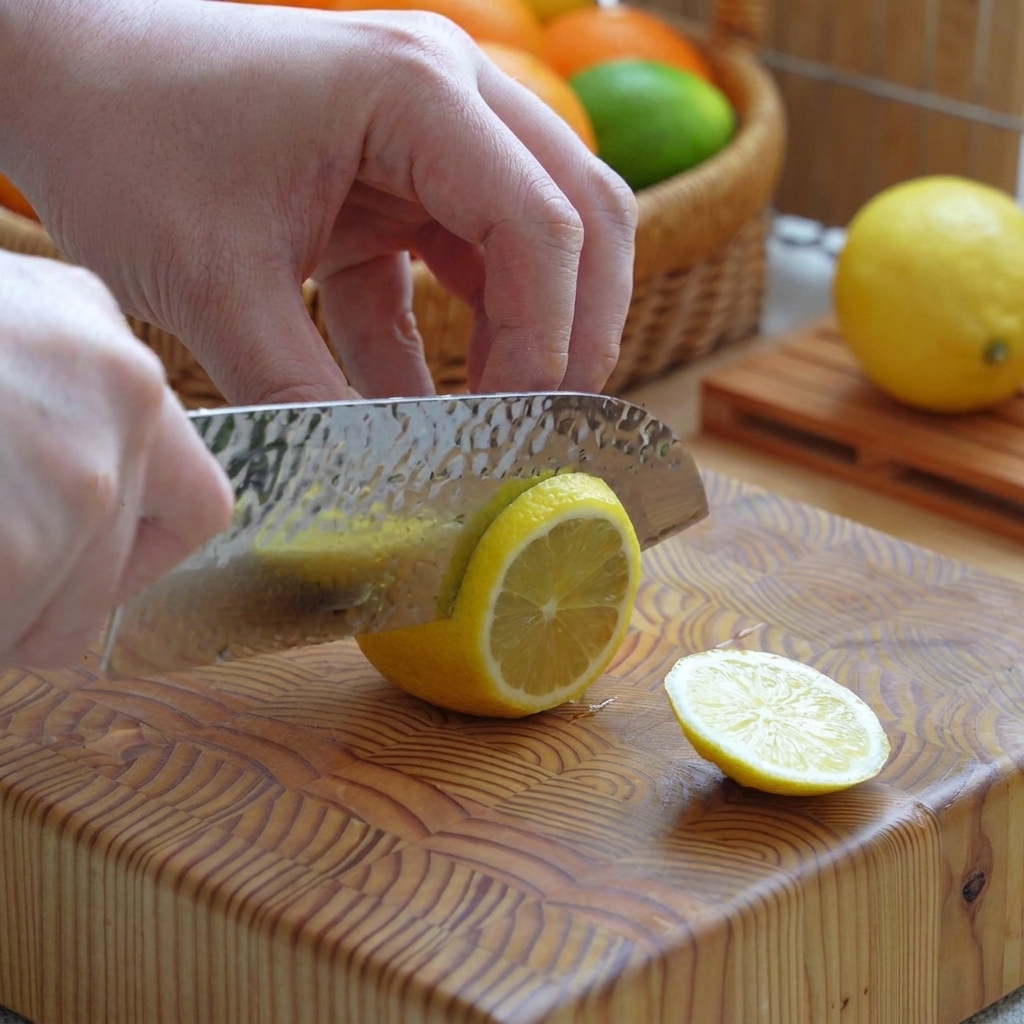 Un limón amarillo siendo cortado en rodajas limpias sobre una tabla de cortar de madera con un cuchillo.