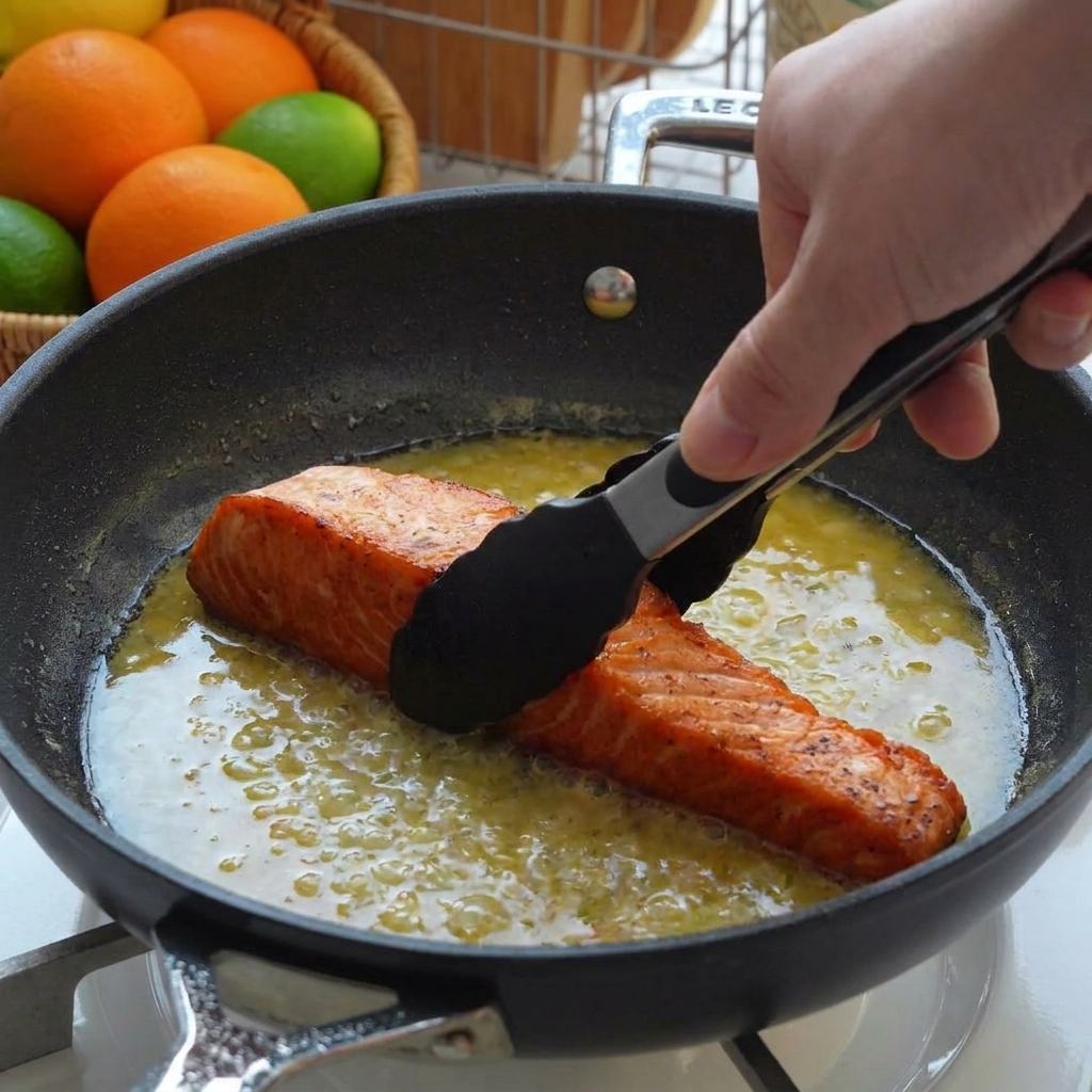 Filetes de salmón sellados siendo colocados en una sartén llena de salsa de mantequilla de limón usando pinzas negras.