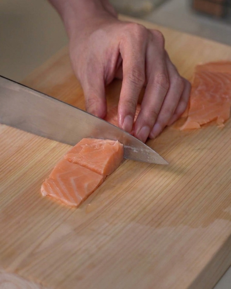 Filete de salmón fresco porcionado en pequeños cubos del tamaño de un bocado sobre una tabla de picar de madera.