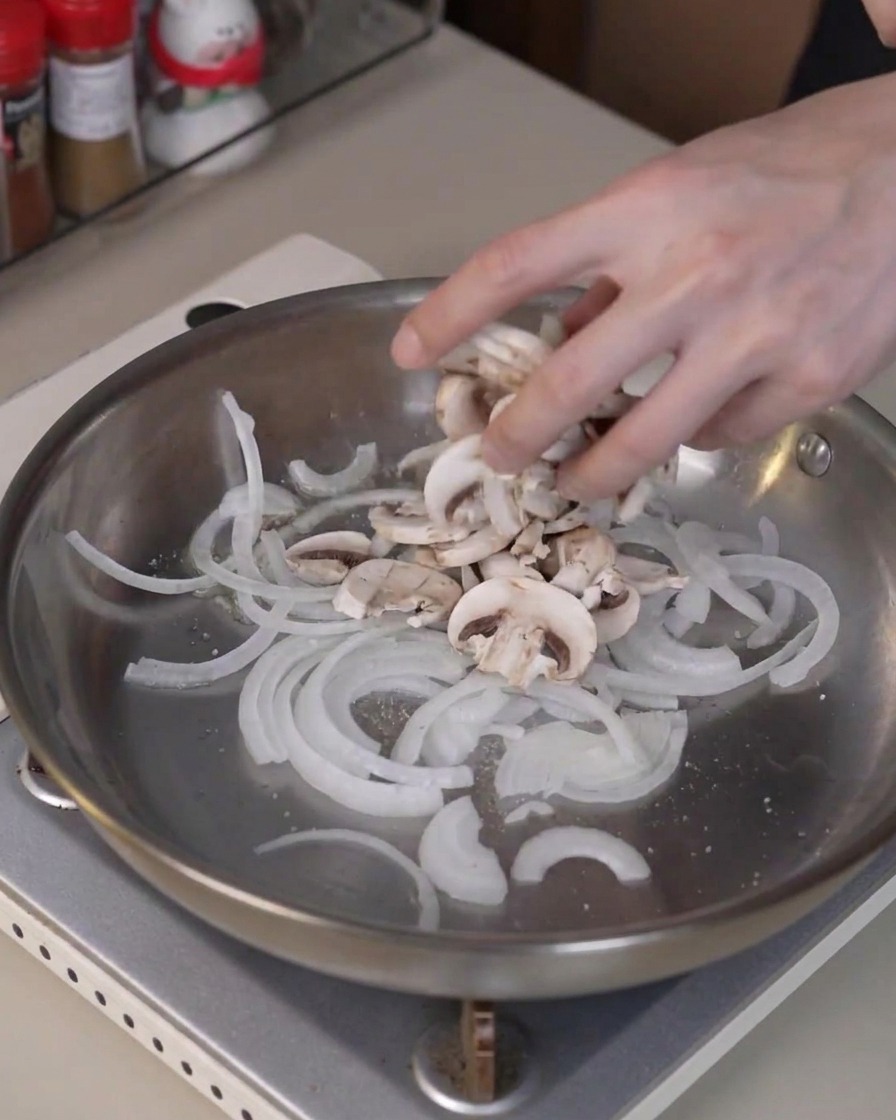 Champiñones en rodajas añadidos a la sartén con cebollas para cocinarse y liberar humedad.