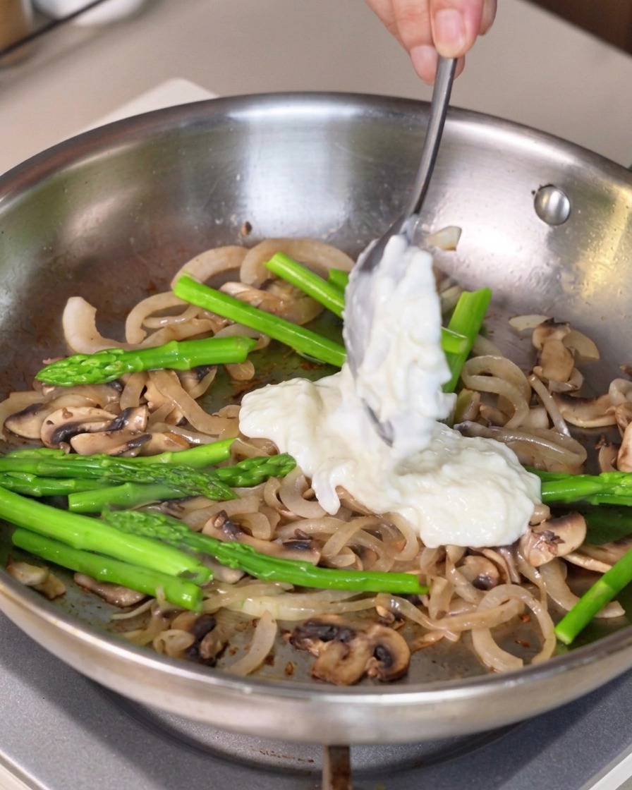 Salsa blanca espesa recogida con una cuchara y añadida a la mezcla de verduras en la sartén.