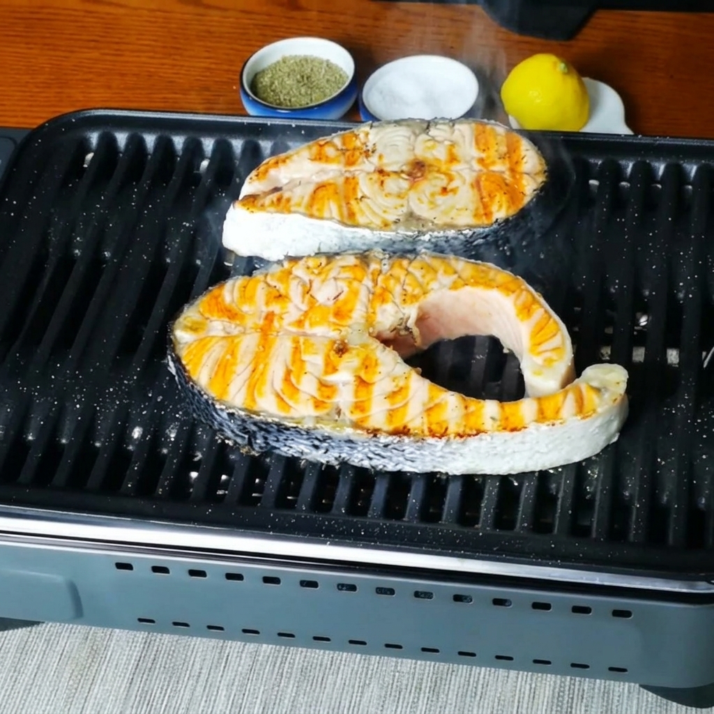 Vista de cerca de los filetes de salmón chisporroteando en la sartén grill después de ser sazonados.