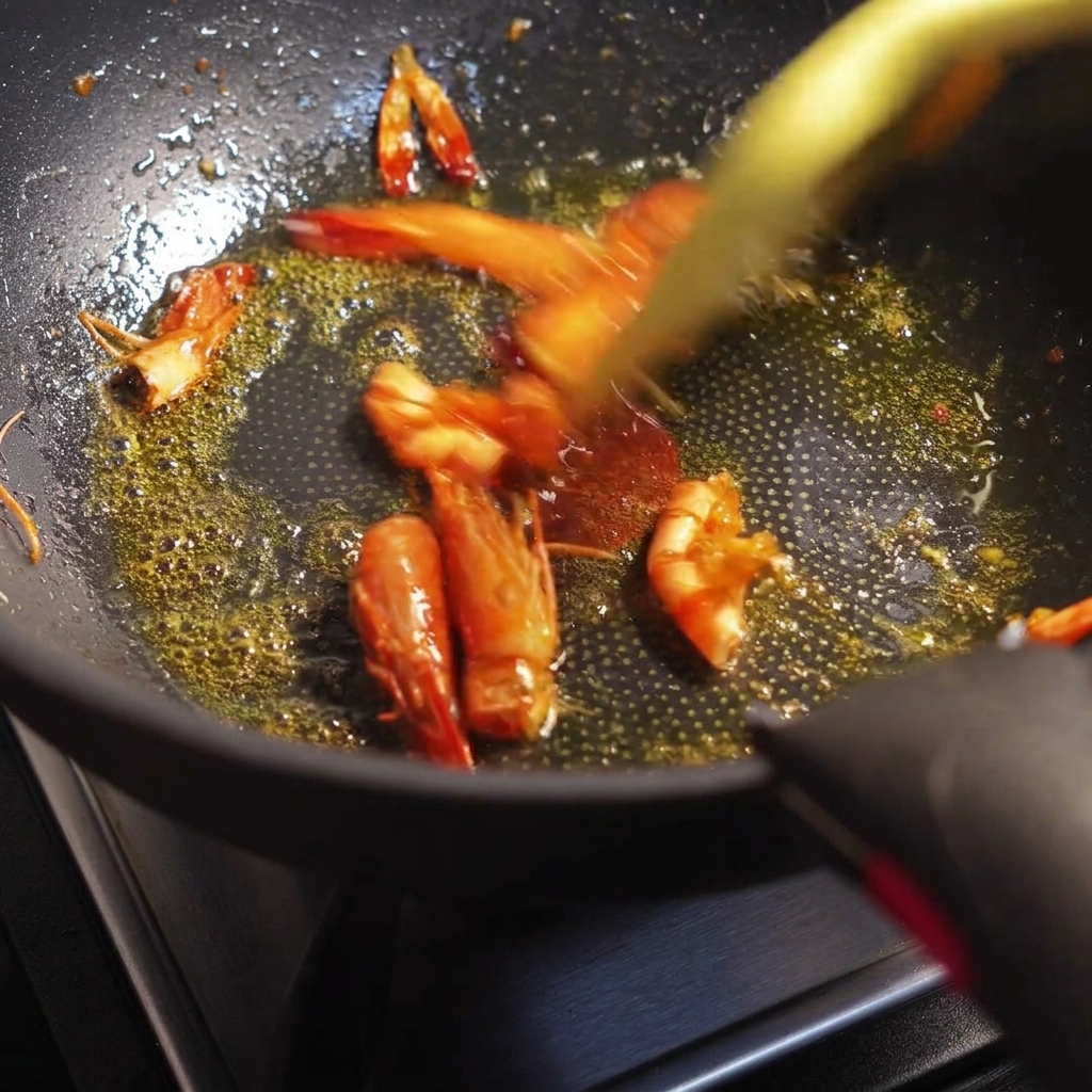 Cabezas y cáscaras de langostino salteándose en una sartén, liberando un aceite de tono anaranjado rojizo.