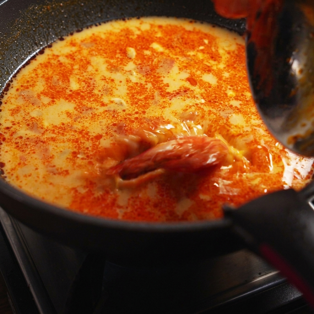Fideos de espagueti cocidos, langostinos y cilantro fresco incorporados a la sartén de salsa a fuego lento.