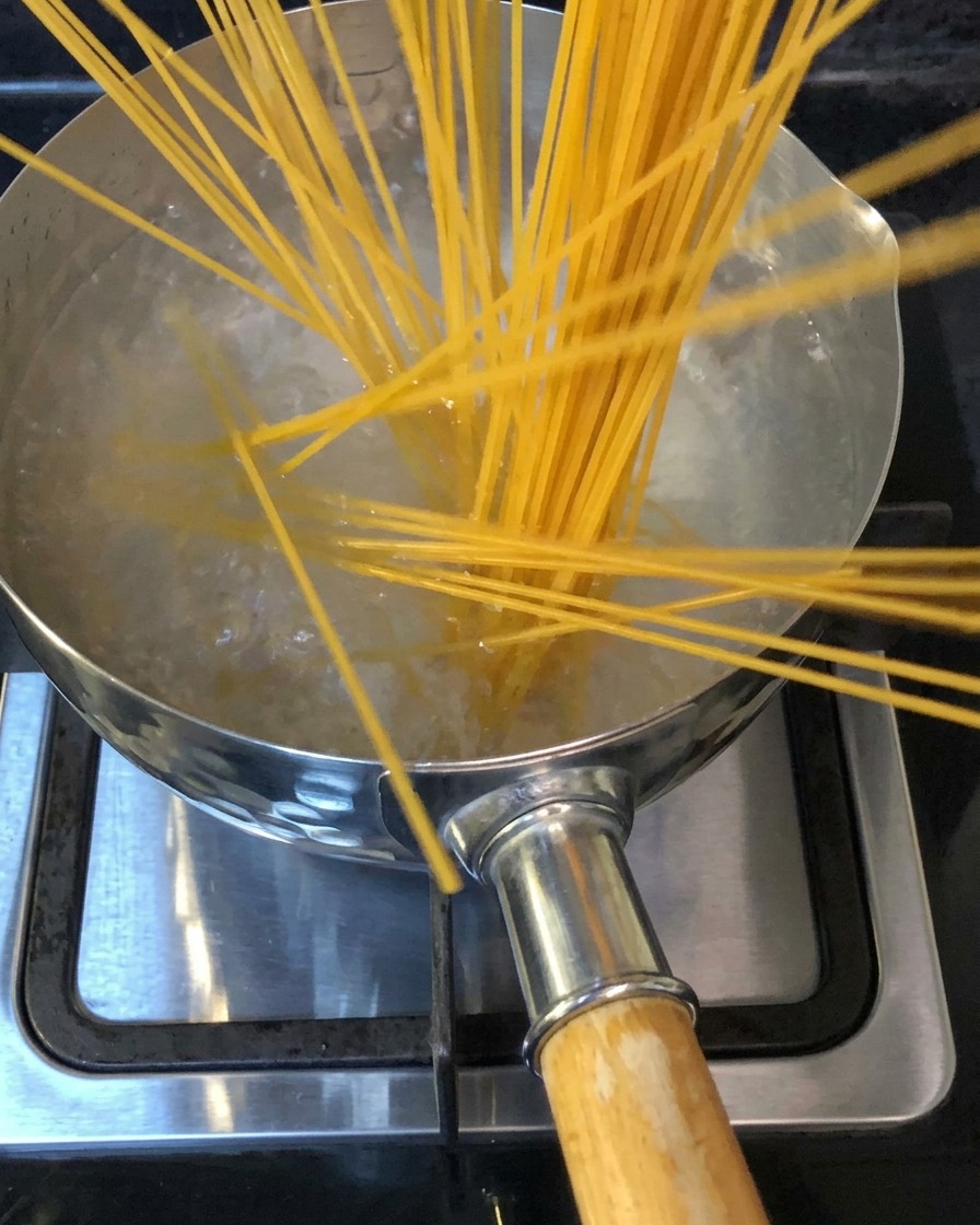 Fideos espagueti sumergiéndose en una olla con agua hirviendo con sal en una estufa.