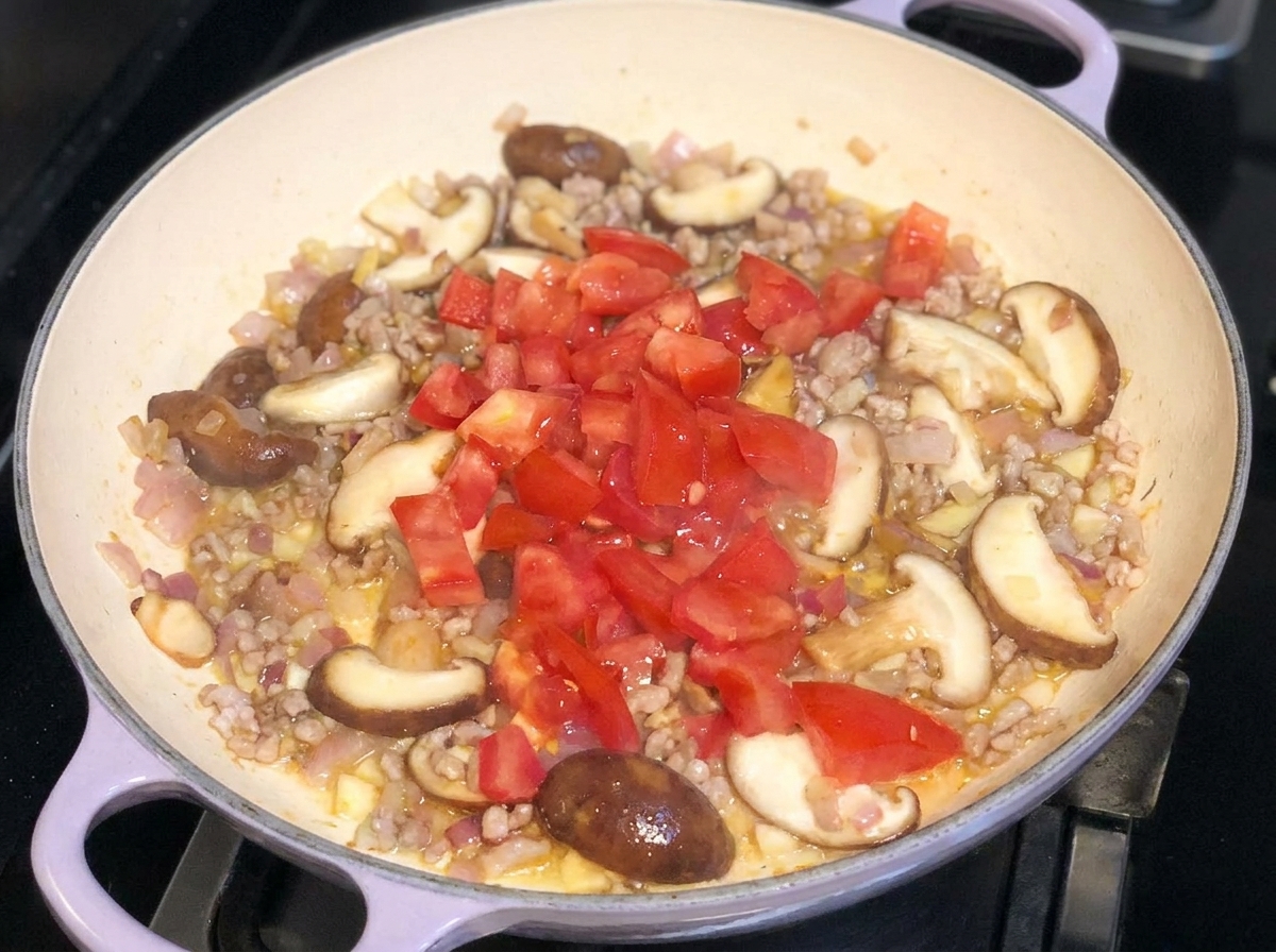 Tomates frescos en cubos añadidos encima de una mezcla salteada de cerdo, cebollas y champiñones en una sartén.