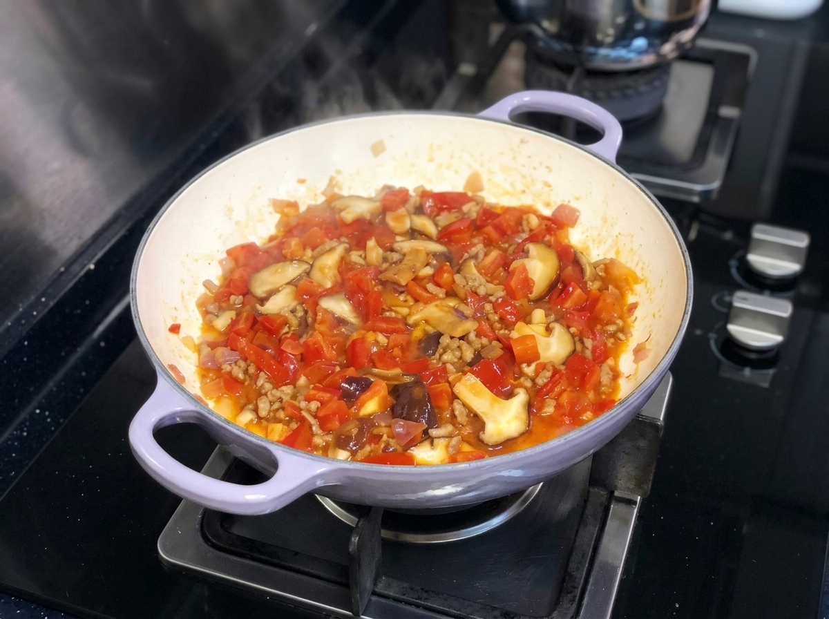 Una mezcla vibrante de tomates picados, cebollas y champiñones shiitake hirviendo a fuego lento juntos en una sartén en una estufa.